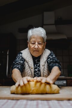 Senior female standing at table in cozy kitchen and kneading raw dough while preparing pastry for cooking domestic Italian tortellini