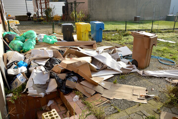 Garbage and cardboard dump in the backyard. On the street there are black, yellow, blue and brown...