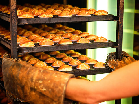 Crop unrecognizable baker in gloves arranging rack with freshly baked muffins for cooling while working in industrial bakery