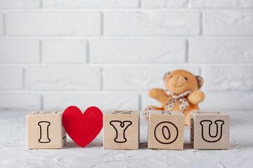 I love you. A declaration of love. Wooden cubes. A teddy bear. White brick wall. Background for Valentine's Day. Copy space.