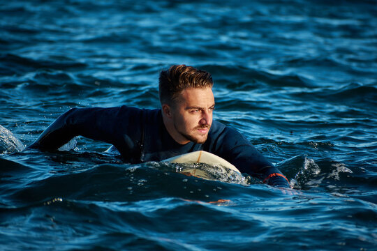 Determined male surfer on surfboard swimming in blue sea on sunny day and looking away