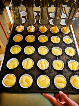 From above cropped unrecognizable baker hands holding tray in automatic industrial dough filling machine used during process of muffins production in professional bakery