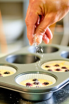 Crop unrecognizable confectioner sprinkling sugar powder into dough with berries in baking form while preparing muffins in kitchen