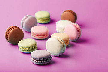 Colorful French macaroni cookies are scattered on a pink background.