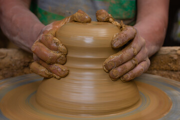 Wet and muddy hands of a craftsman shaping a clay vase on a pottery wheel. Artisan from Ráquira, Colombia. Shallow depth of field