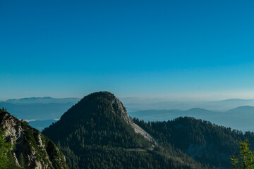 Fototapeta premium A panoramic view on the Alps from the top of Mittagskogel in Austria. Clear and sunny day. Sharp peaks around. A bit of haze in the valley. Outdoor activity. Alpine mountain chains in the back. Calm
