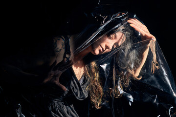 From above of female lying on black background under sheet of cellophane and showing concept of plastic pollution