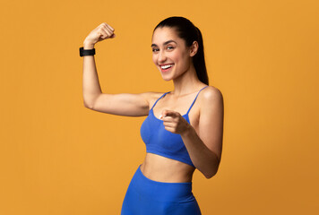 Happy sporty woman showing biceps and pointing to camera