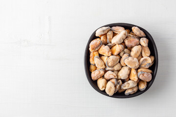 Frozen peeled mussels in black bowl on white wood table, top view