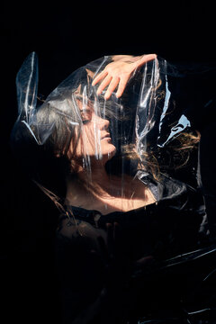From above side view of dead female lying on black background under sheet of cellophane and showing concept of plastic pollution