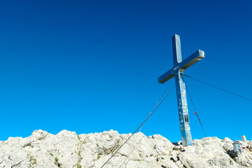 Fototapeta na wymiar A metal cross of the top of Mittagskogel in Austrian Alps. Clear and sunny day. Endless mountain chains. Outdoor activity. Barren top of the mountains, lush lower parts. Achievement and completion