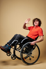 Obraz na płótnie Canvas joyful disabled guy on wheelchair say hello at camera, smiling, have fun alone, isolated studio portrait