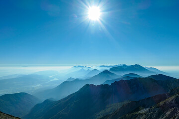 A close up view on the Alpine chains shrouded in the morning fog, seen from the top of Mittagskogel in Austria. Clear and sunny day. Sharp peaks around. Sun is shining above the high peaks. Serenity