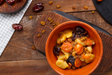 Jewish cuisine dish sweet tsimes with carrot dates in a clay plate on a wooden board.