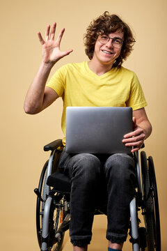 handicapped male on wheelchair say hello at camera sitting on wheelchair with modern laptop, working online , smiling.