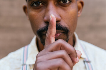 Crop African American male covering mouth with finger and showing silence sign while looking at camera