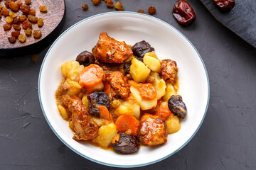 Jewish cuisine dish sweet tsimes with dates, carrots and turkey meat in a white plate on a black board on a concrete background near raisins and dates.