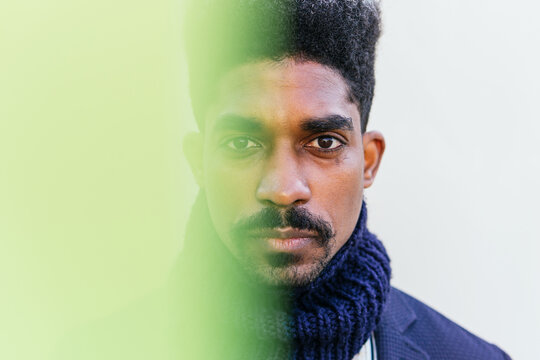 Through yellow light filter of carefree African American male with curly hair standing in white wall looking at camera