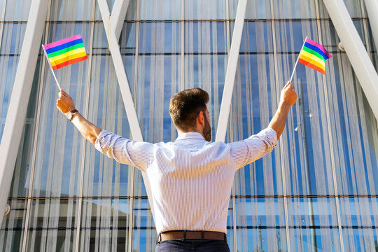 Back view low angle of homosexual male standing on street with paper LGBT flags and looking away