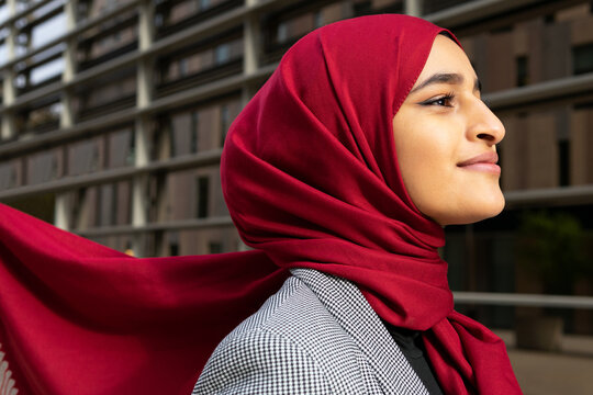 Side view of young content Arab female wearing red hijab standing on street and looking away