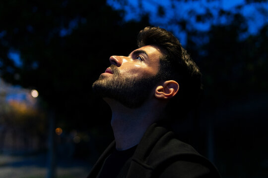 Side view of bearded male contemplating and looking up while standing on dark street
