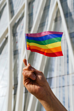 Low angle of cropped unrecognizable homosexual male standing on street with paper LGBT flags