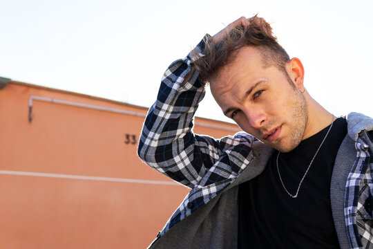 Confident young hipster guy in casual checkered shirt looking at camera while standing against orange wall