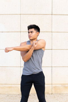 Confident athletic Asian male in sportswear standing on street and stretching arms before active training while looking away