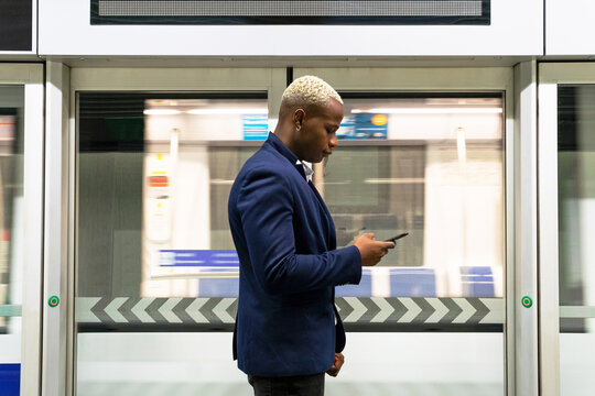 Side view of serious African American businessman standing in subway train and messaging on smartphone while commuting to work