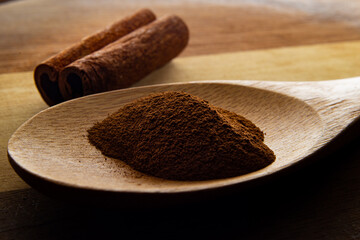 Colher de madeira com pó de canela e pedaço de canela sobre uma tábua de madeira.