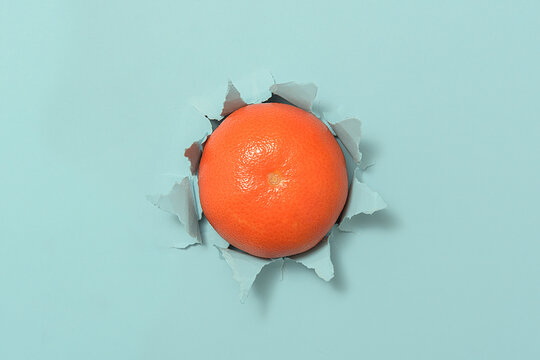 A Ripe Tangerine Through Torn Blue Paper.