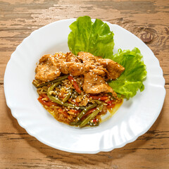 Vegetables with rice and chicken in a pan-Asian sauce on lettuce leaves on a wooden table in a plate.
