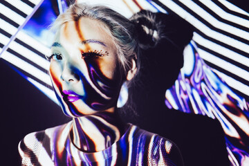 Young female asian model with stylish eyes makeup and shadows on face standing in studio illuminated with colorful spotlights