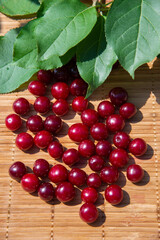 Red cherry berries and green leaves on a bamboo napkin are laid out in the form of a berry shape. \the sign of the red berry. The concept of healthy vitamin berries and fruits