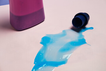 Top view of liquid detergent spilled from plastic cap on pink background in studio