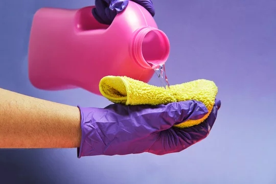 Crop anonymous person with plastic bottle pouring liquid detergent in a rag in studio