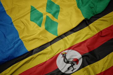 waving colorful flag of uganda and national flag of saint vincent and the grenadines.