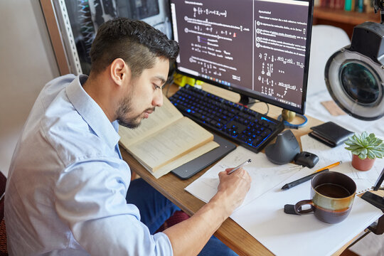 Side view high angle of crop male student sitting at table and writing on sheet of paper and preparing for exam