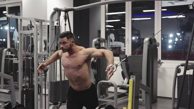 Muscular bodybuilder at cable crossovers fitness men pumping up muscles.