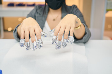 Unrecognizable crop female client sitting at table in nail salon and removing gel polish with foil