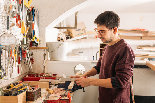 Side view of crop faceless male carpenter using metal angle and wooden plank while working at workbench in bright garage
