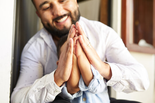 Hispanic father teaching cute toddler praying with clasped hands while sitting at home