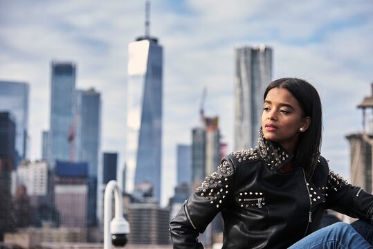 Thoughtful African American female in leather jacket sitting on street in New York and enjoying cityscape