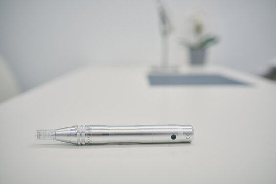 Derma pen with micro needles placed on white table for dermatology treatment in modern beauty clinic