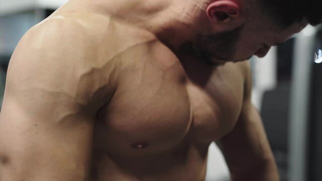 Topless muscular male sportsman doing bodybuilding triceps extensions in a crossover machine