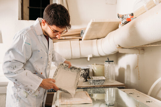 Side view of serious male artisan pouring liquid gypsum in wooden form for shaping material while creating artwork in workshop