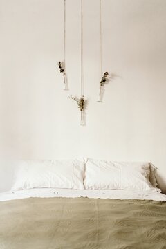 Minimalist interior of bedroom with soft bed and bohemian handmade decorations hanging on white wall