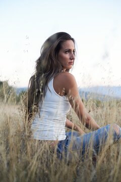 Side view calm slim brunette with long hair sitting alone on meadow in countryside looking away in dreams
