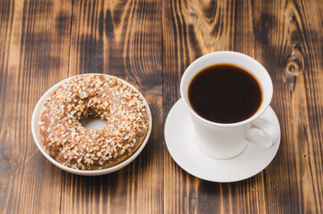 White cup of black coffee and donut with nuts.