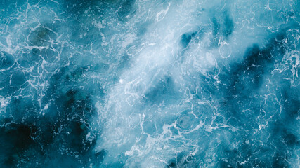From above aerial view of turquoise ocean water with splashes and foam for abstract natural background and texture
